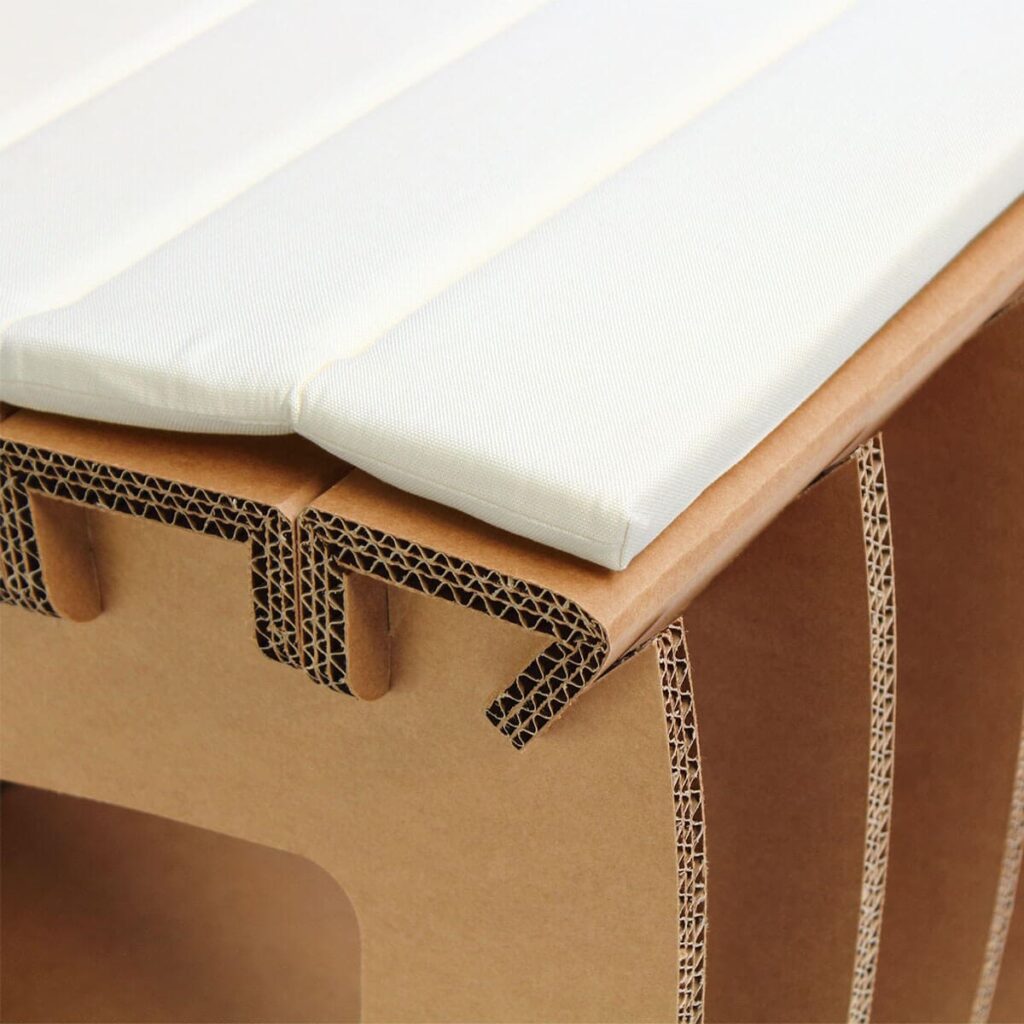 Chaise en carton écologique avec siège et accoudoirs en tissu blanc, conçue pour l’aménagement d’espaces professionnels comme les bureaux ou salles de pause, structurée par des panneaux cartonnés renforcés et ergonomiques - Le Meuble en Carton une marque du groupe Natur Design