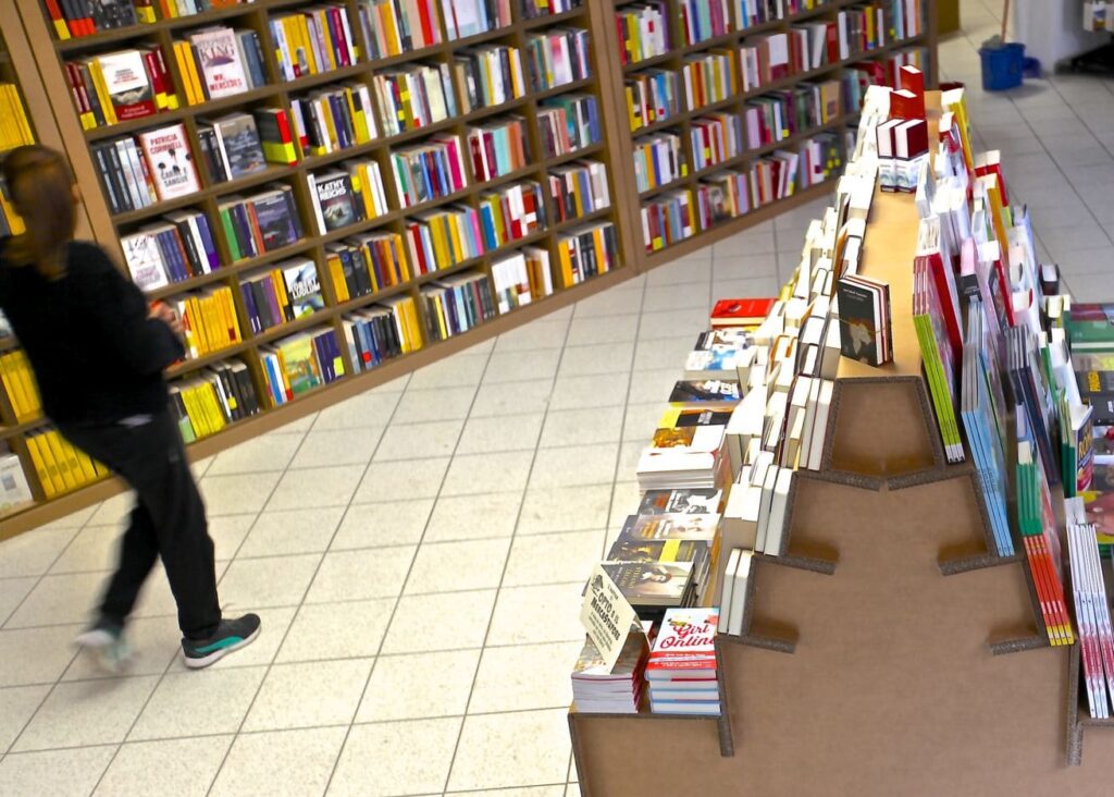 Présentoir à livres en carton pour l'aménagement de magasins, structuré avec des supports métalliques, affichant une sélection variée de livres et magazines organisés sur plateau cartonné - Le Meuble en Carton une marque du groupe Natur Design
