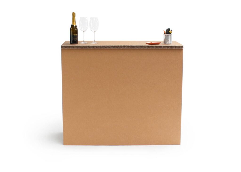 Banque d'accueil en carton écologique avec plateau décoré d'une bouteille de champagne et deux verres à vin, ainsi que des accessoires bureautiques comme un stylo et une boîte de crayons sur le dessus, idéale pour les espaces professionnels ou événements - Le Meuble en Carton une marque du groupe Natur Design