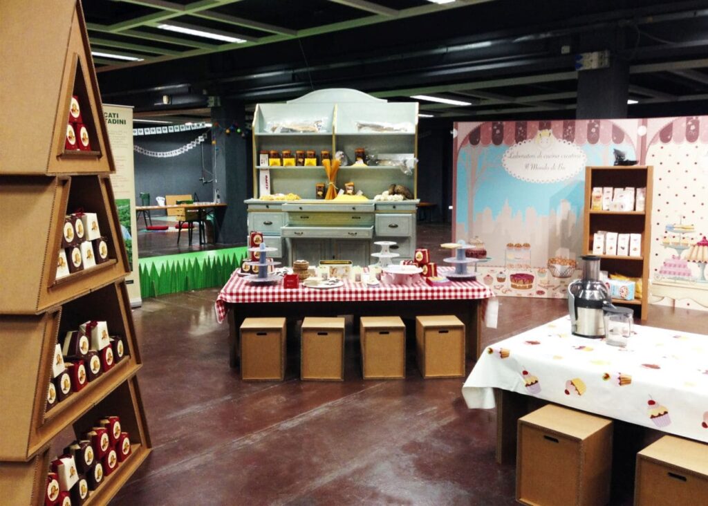 Étagères en carton NANDA pour présentation d'expositions événementielles : structure modulable en carton écologique avec placards et rangements décorés, intégrée dans un stand cartonné aux côtés de tables et présentoirs de pâtisseries et produits gourmands pour salons professionnels ou espaces de scénographie festive - Le Meuble en Carton une marque du groupe Natur Design