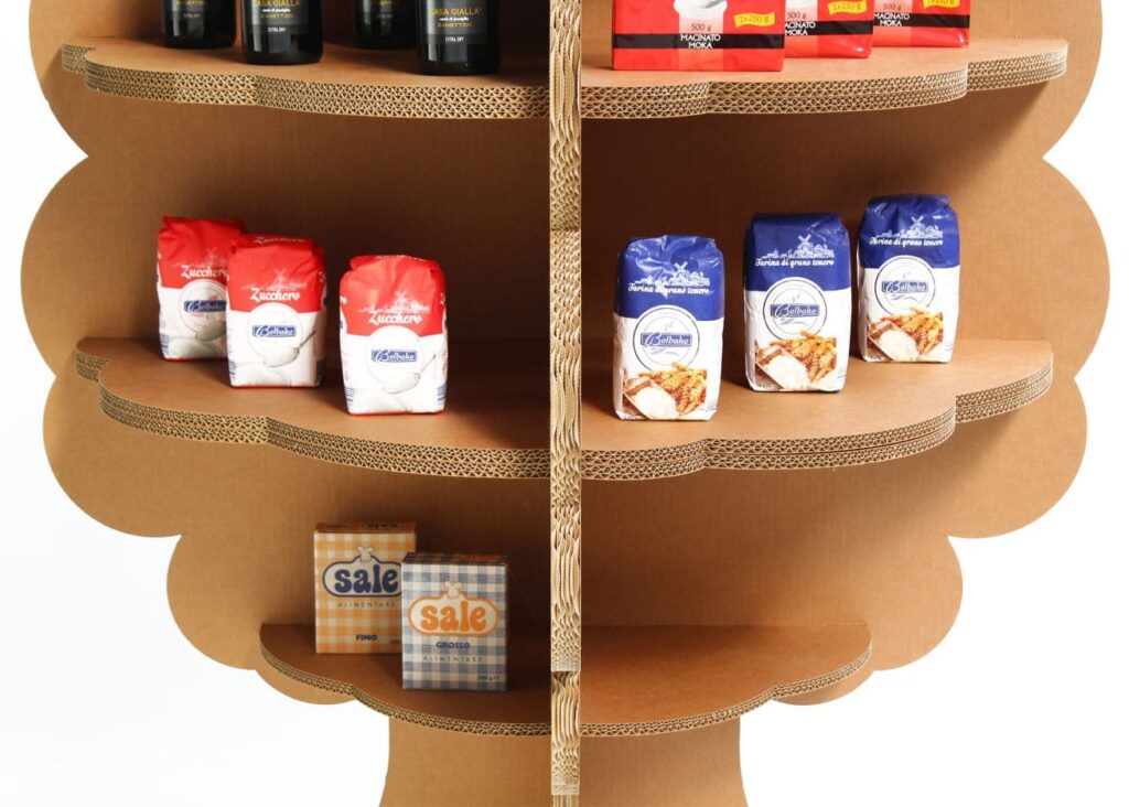 Présentoir en carton KAILA pour l’aménagement de magasins, structuré avec étagères en carton ondulé et plateau visible, accueillant des produits alimentaires comme sachets de sucre, farines et boissons en bouteille. Idéal pour organiser les rayons de produits secs ou liquides dans un espace commercial ou point de vente - Le Meuble en Carton une marque du groupe Natur Design