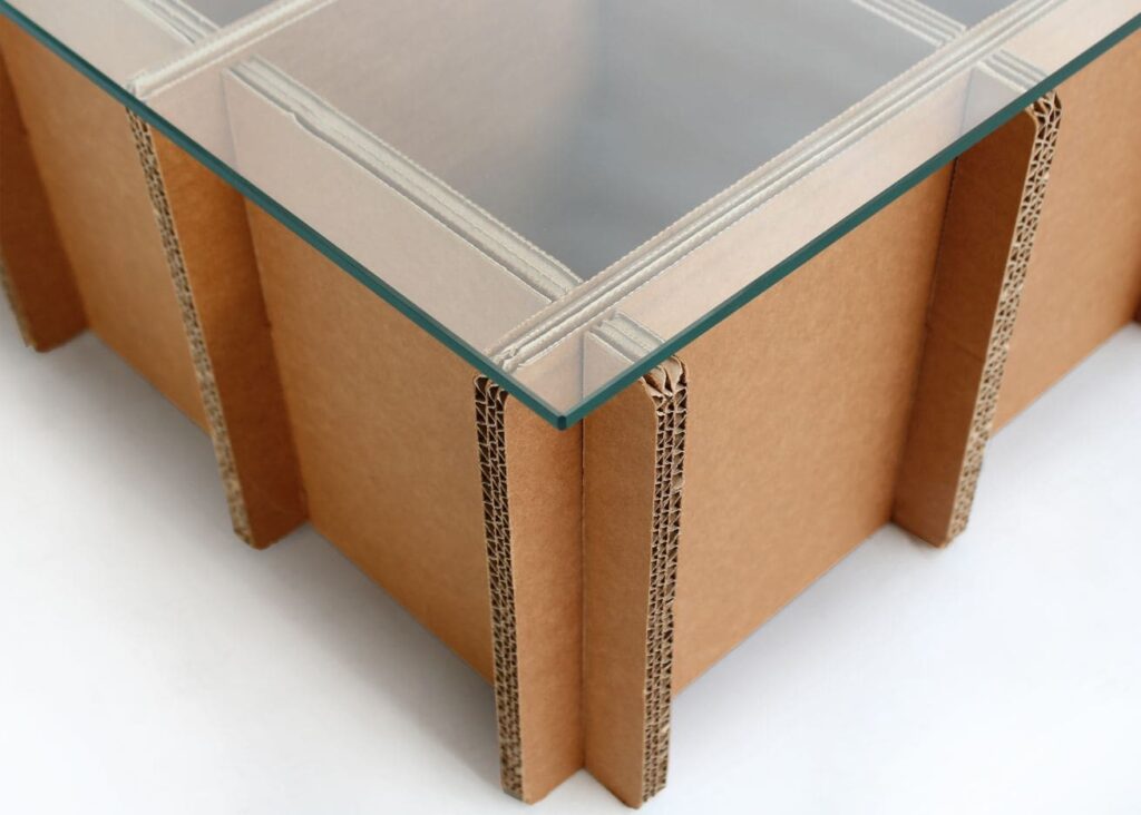 Table basse en carton écologique avec plateau transparent intégré, idéale pour les espaces d'aménagements professionnels comme les bureaux ou les salles de pause. Structure solide composée de panneaux cartonnés renforcés par des tringles métalliques et un support stabilisé en carton ondulé pour une stabilité optimale - Le Meuble en Carton une marque du groupe Natur Design